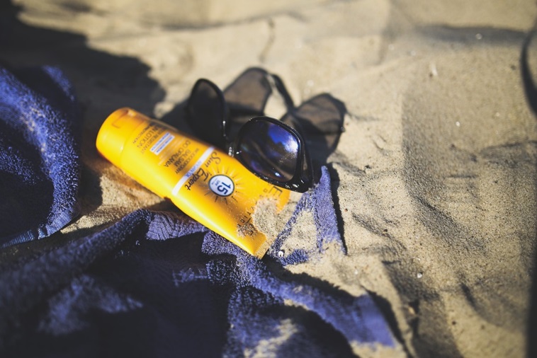 Crème solaire sur une serviette posée dans le sable à côté de lunettes de soleil. réglementation des produits solaires